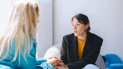 Getty Images Two women sitting in armchairs and talking. Female coach, psychotherapist, psychologist, advisor and patient, client 