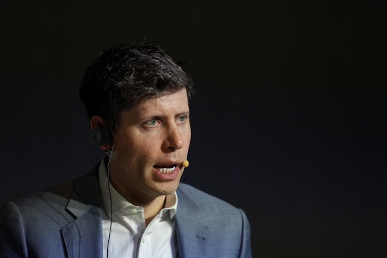 A white man speaks while wearing a headset with a microphone