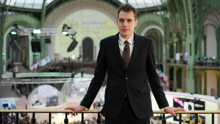 Arthur Mensch, founder of Mistral AI, stands in a suit at the AI Action Summit venue in Paris, looking toward the camera.