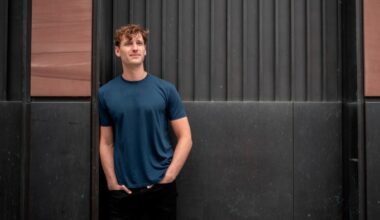Winston Weinberg stands with hands in pockets against a dark paneled wall, looking slightly upward and smiling.