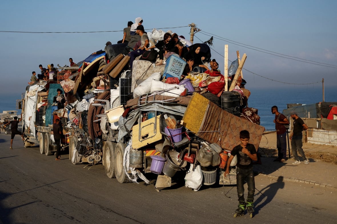People sit atop of a truck with belongings piled on.