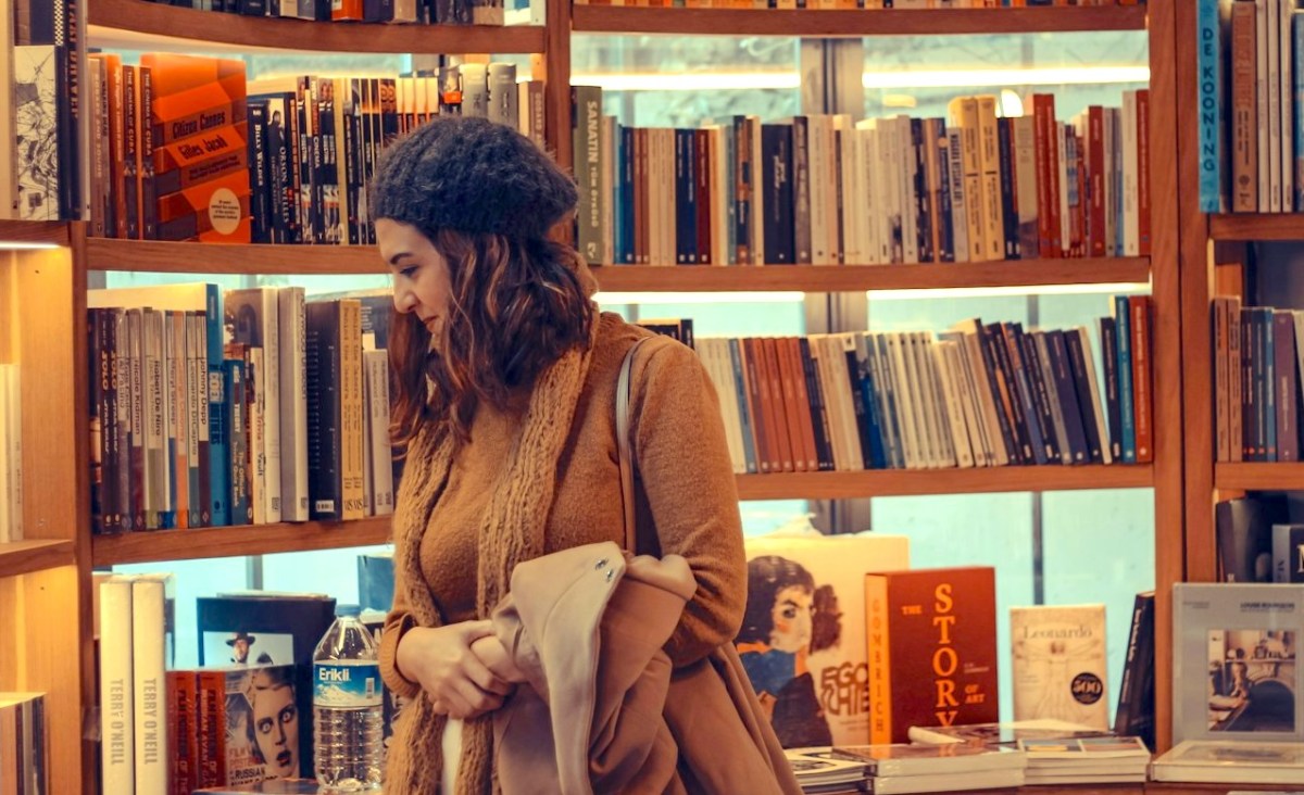 woman in a brown coat reading book in library