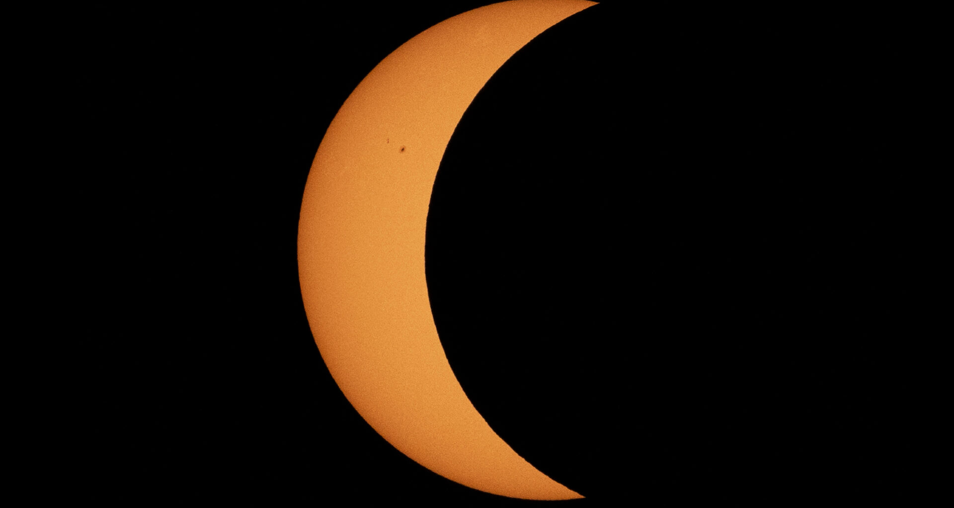 A photo of the sun captured during a partial solar eclipse. The silhouette of the moon covers the majority of the sun, transforming it into a crescent, or sickle shape.