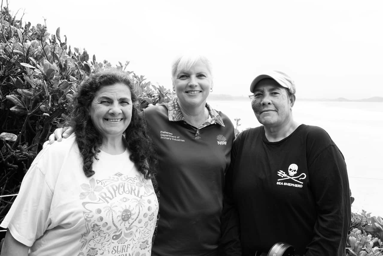 A black and white photo of three middle-aged women standing near the ocean.