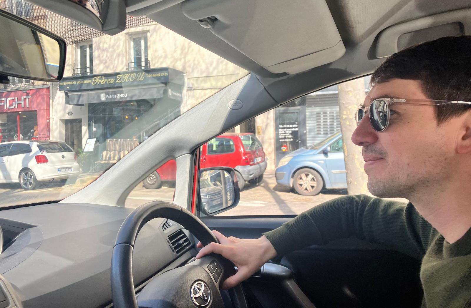 Hugo Daniel driving his car, with a street view visible through the windshield.