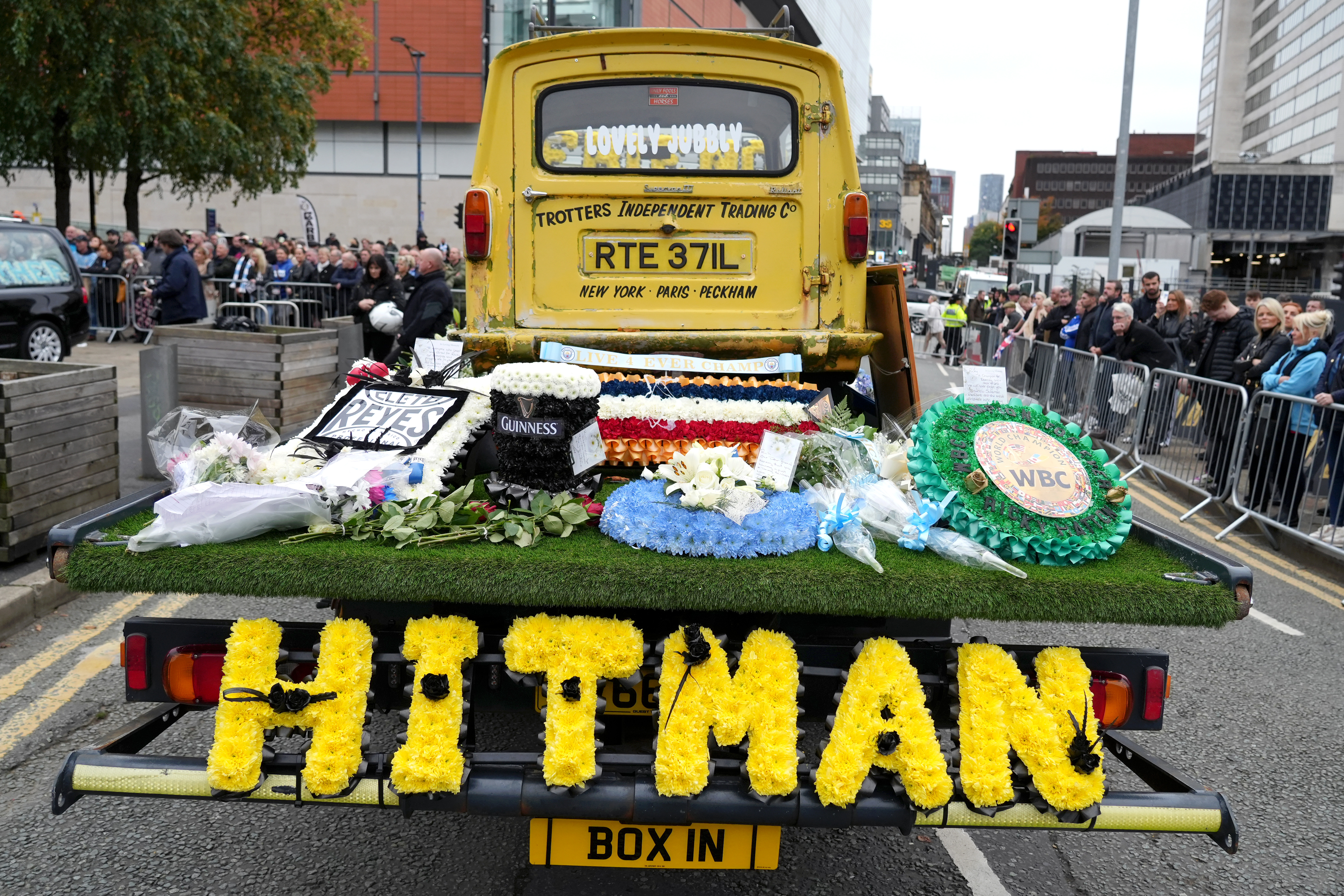 The funeral procession for Ricky Hatton, with floral tributes on the back of a yellow truck.