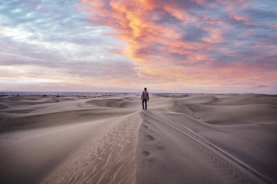 One man standing on top of a sand dune at sunrise, Grand Canary, Spain showing how to manage stress and build resilience.
