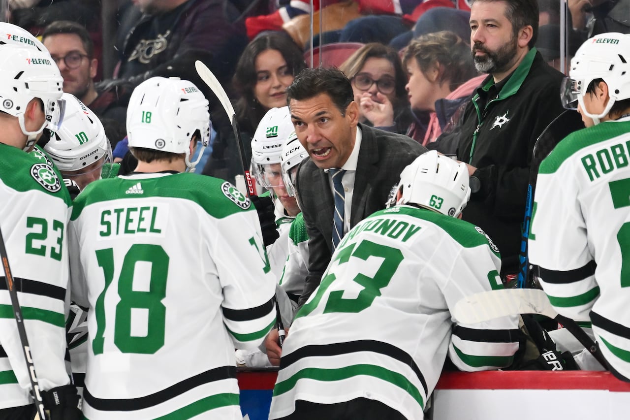 A hockey coach is shown talking to his players, who are wearing white, green and black jerseys.