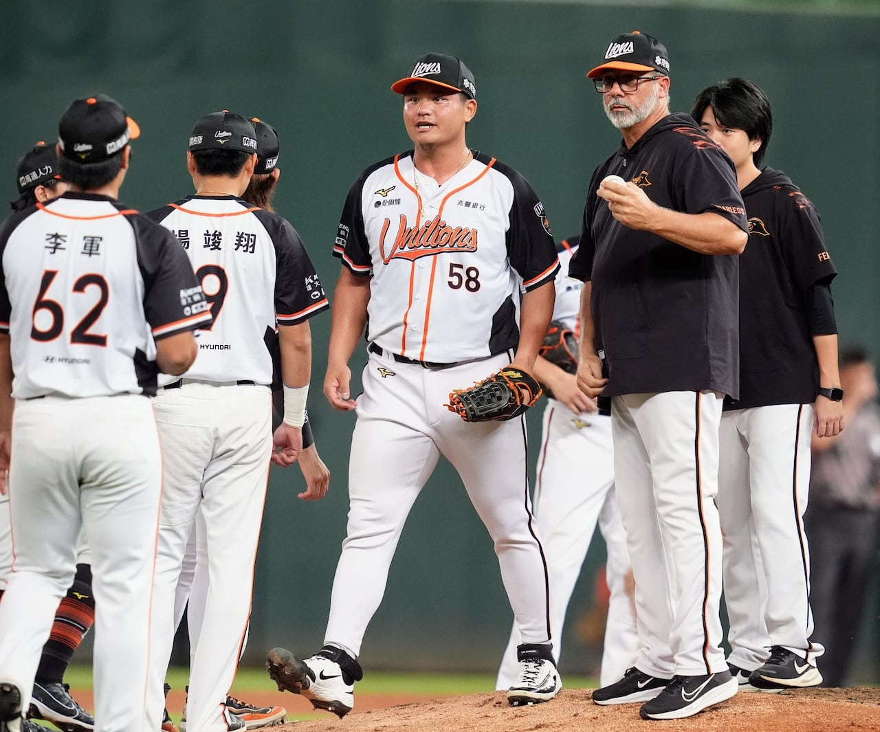 A pitching coach holds on to the baseball as several players gather on a mound.
