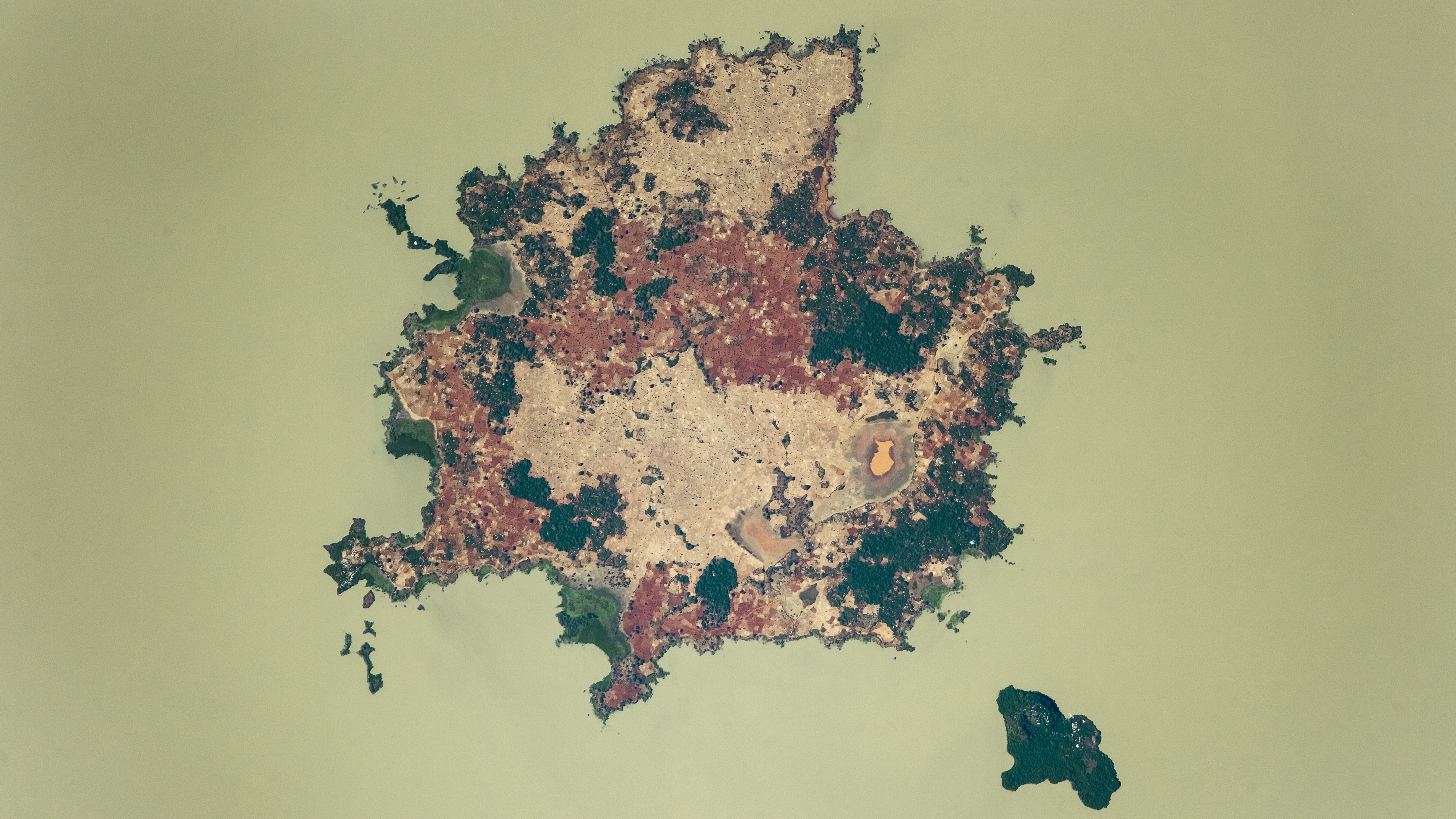 An astronaut photo of a large island and a smaller island in a milky green lake