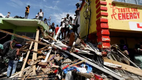 Reuters People stand on top of the debris of a building in Jamaica. 