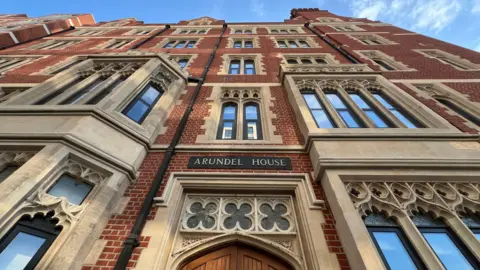 Stuart Woodward/BBC Arundel House is a red brick building with sandstone window surrounds. It is a five-storey building, with a sign reading "Arundel House" positioned above the main doorway. There is blue sky and white clouds above