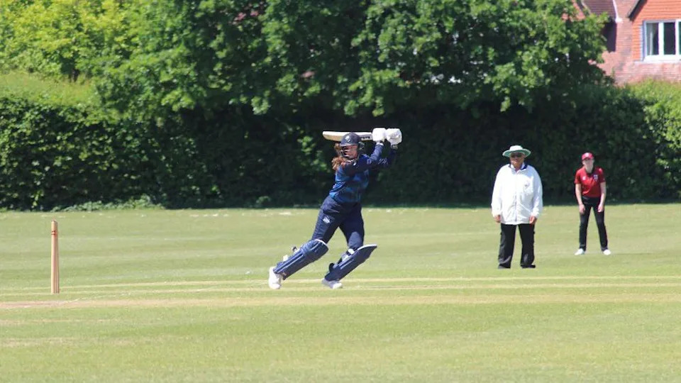 Libby uses her quick footwork to play the ball into the leg-side. Her right foot is on tip-toes whilst her left is planted, helping the ball around the corner towards the square-leg umpire. Libby is wearing a navy blue cricket kit with matching helmet