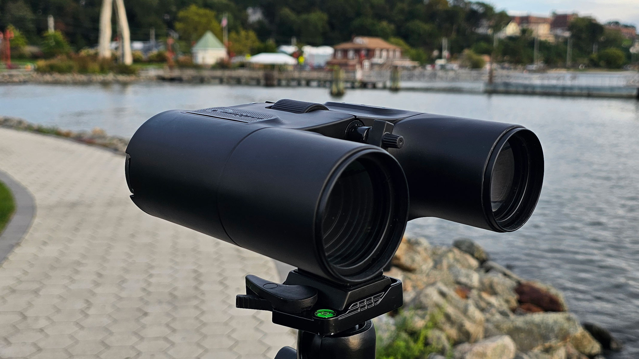 A side-front view of the Unistellar Envision smart binoculars with water and houses in the background.