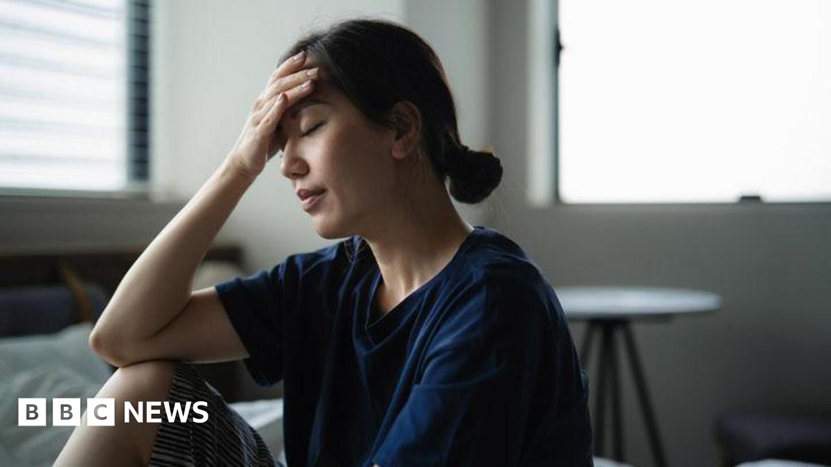 A man with grey hair on the sides of his head and glasses smiles at the camera. He is wearing a grey suit jacket.