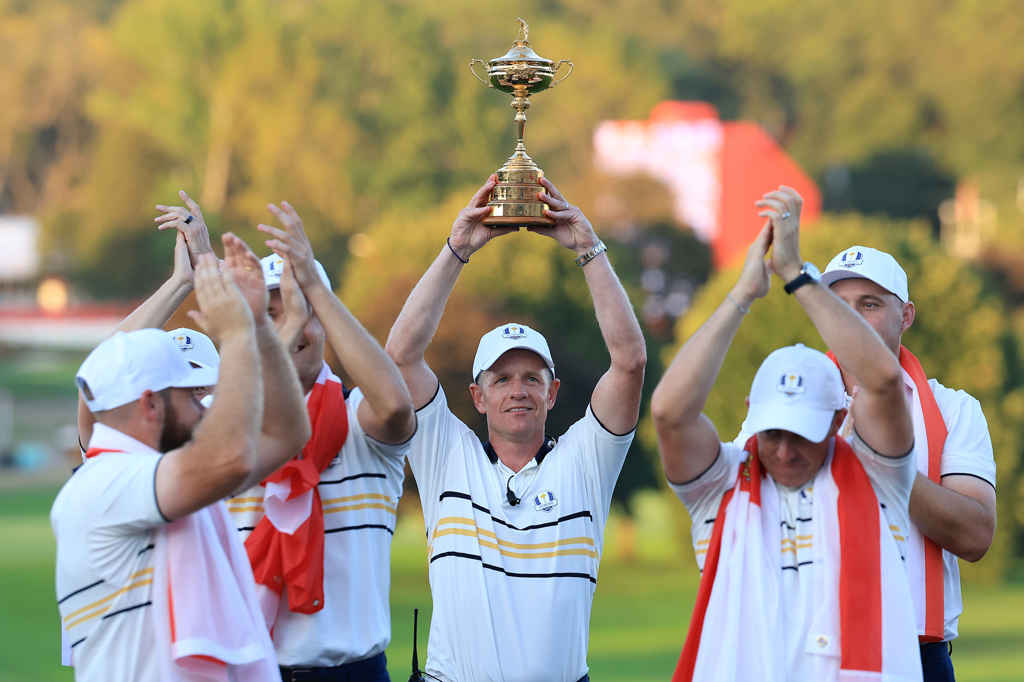 Luke Donald raising the Ryder Cip trophy aloft in victory, as members of Team Europe clap their hands around him
