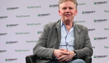 A man in a suit jacket sits at a TechCrunch speaking event