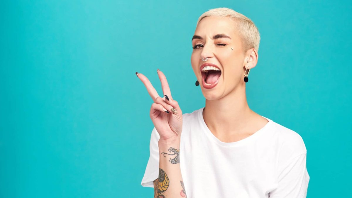 A tattoed woman holds two fingers up in a peace sign.