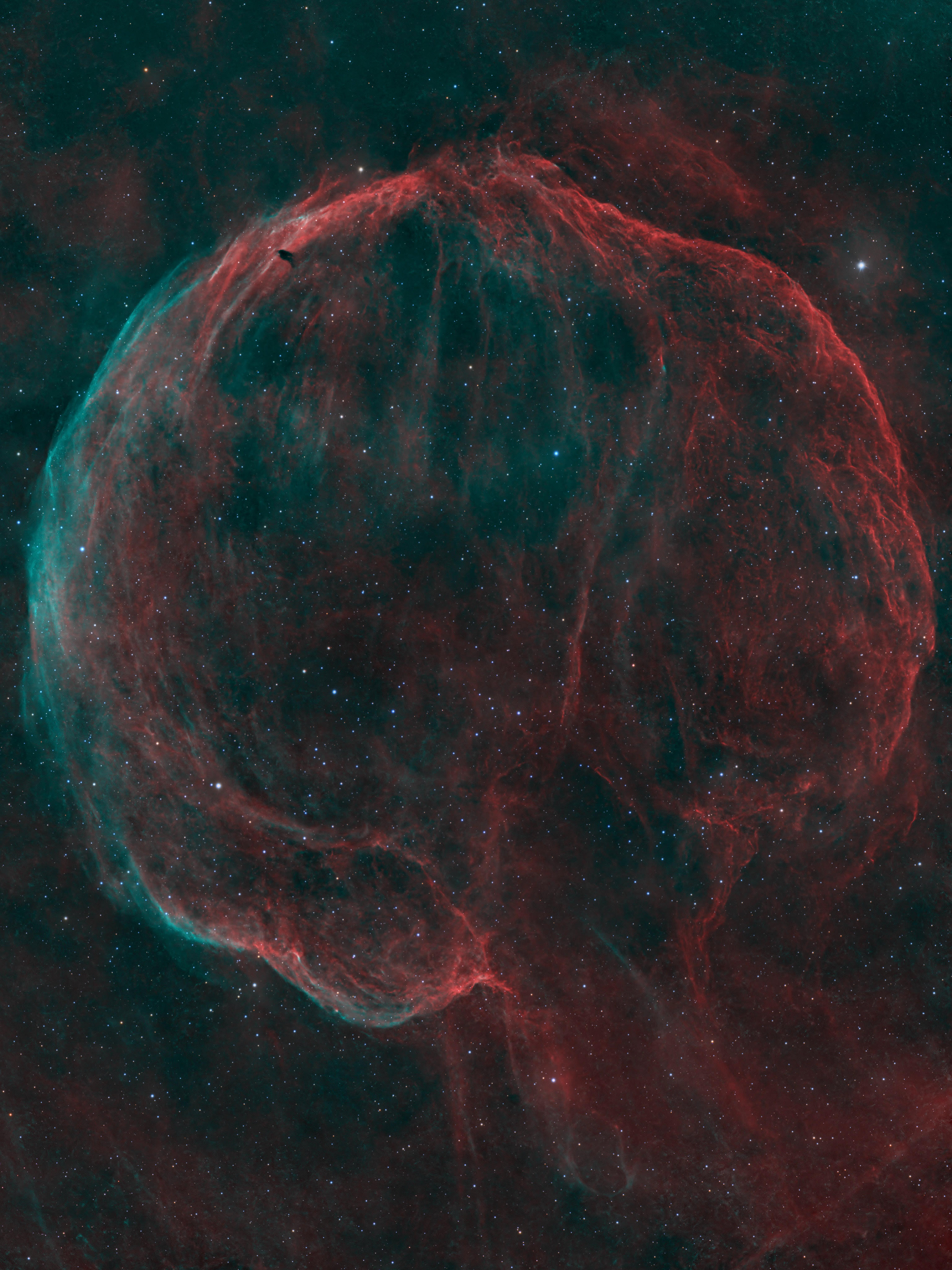 A deep space nebula scene showing a bubble-like shell of cosmic dust and gas shining red and blue against a black sky peppered with bright stars.