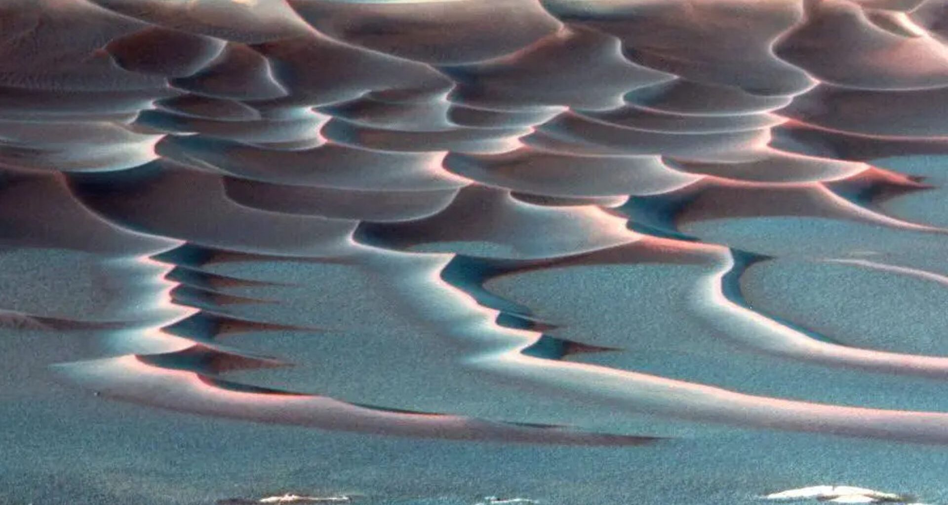 A false color image shows red sand dunes streaking across a blue surface