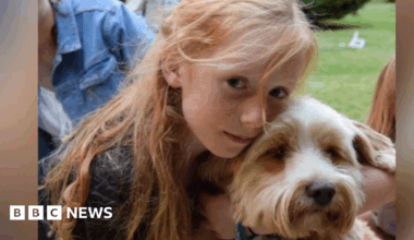 A picture of Ruth Szymankiewicz, who has long ginger hair, cuddling a terrier dog.