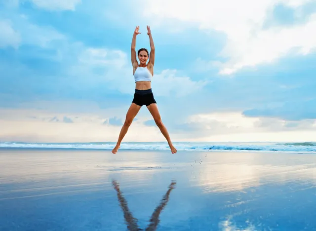 fit woman doing jumping jacks at the beach in shallow water