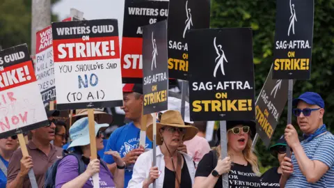 Reuters Members of the Hollywood's actors and writers unions walk with signs in Los Angeles, California. They wave signs that say "On Strike" and others blasting AI. 