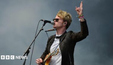 Kodaline play on stage. There is a banner behind them which says 'Kodaline'.