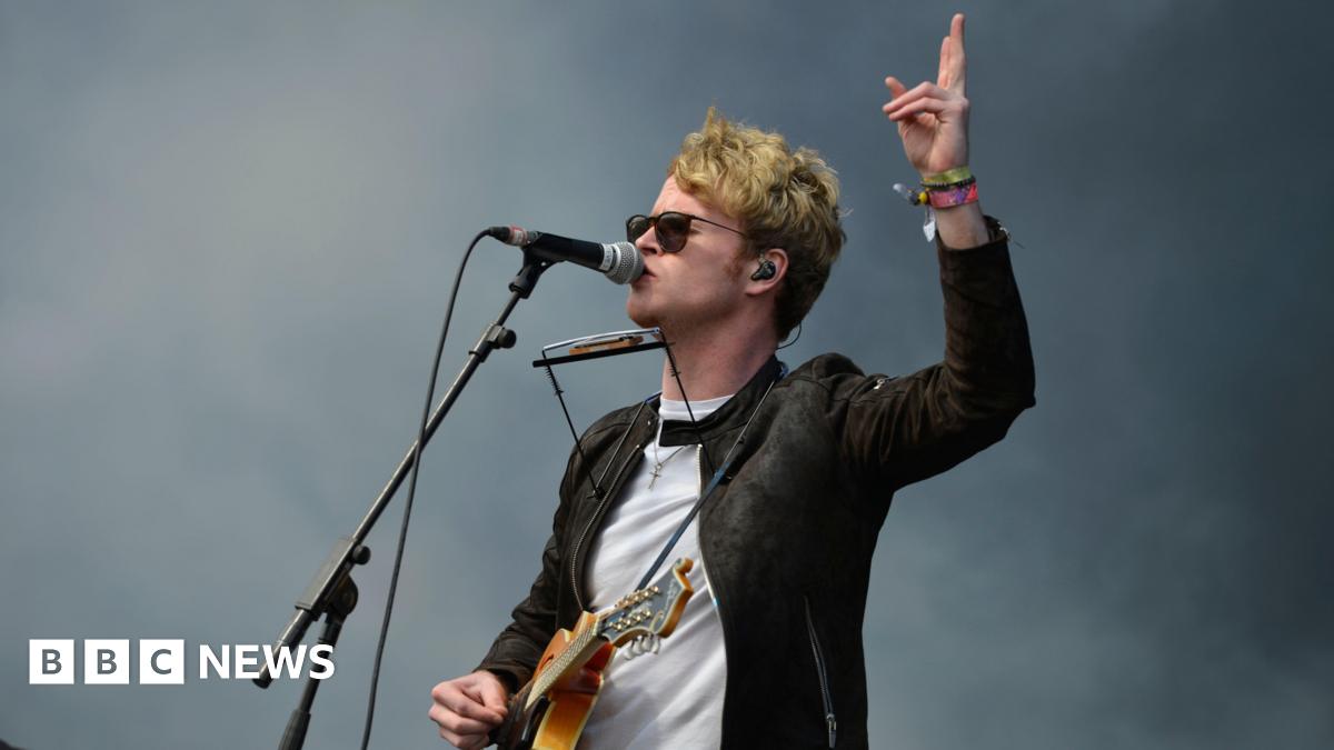 Kodaline play on stage. There is a banner behind them which says 'Kodaline'.