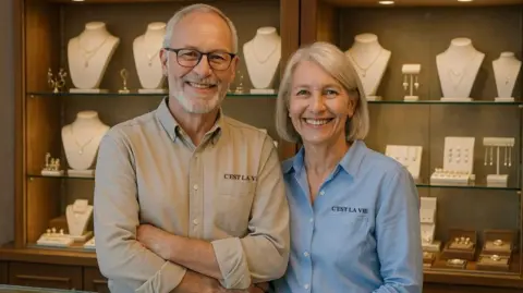 C'est La Vie A man and a woman are smiling and standing in front of a counter filled with jewellery 