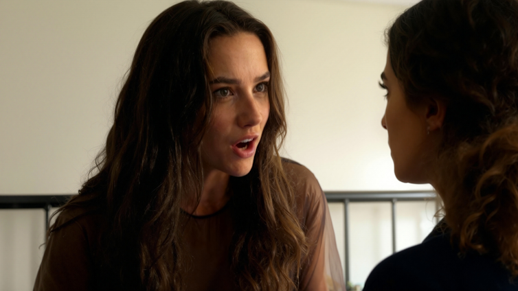 An AI-generated character is speaking to another person in a movie still.