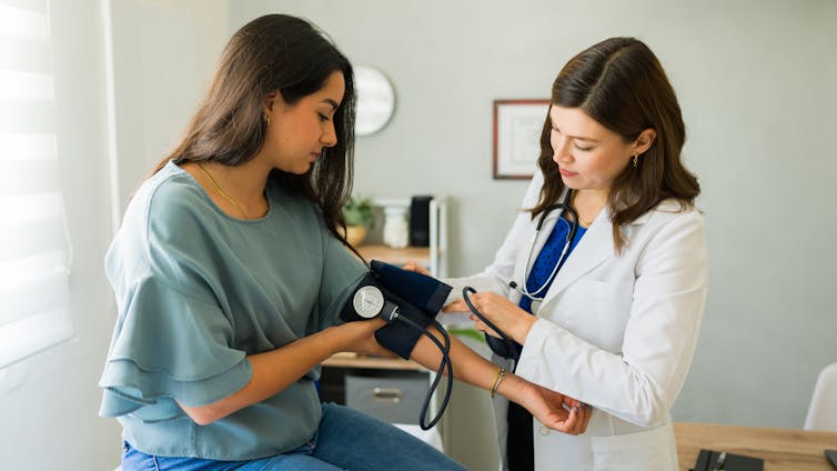 A young woman has her blood pressure checked by a female doctor.