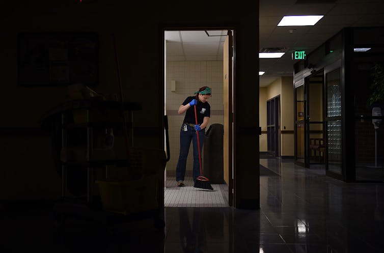 A dark hallway in a hospital with a young woman mopping the floor.