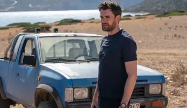 Jack Whitehall in a still from Malice. He's in front of a battered blue pickup near a lake