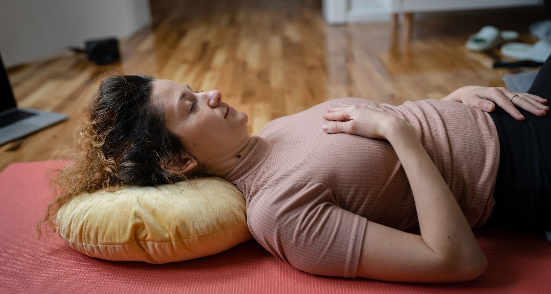 woman lying on her back with a yellow cushion behind her head with one hand on her chest and abdomen.