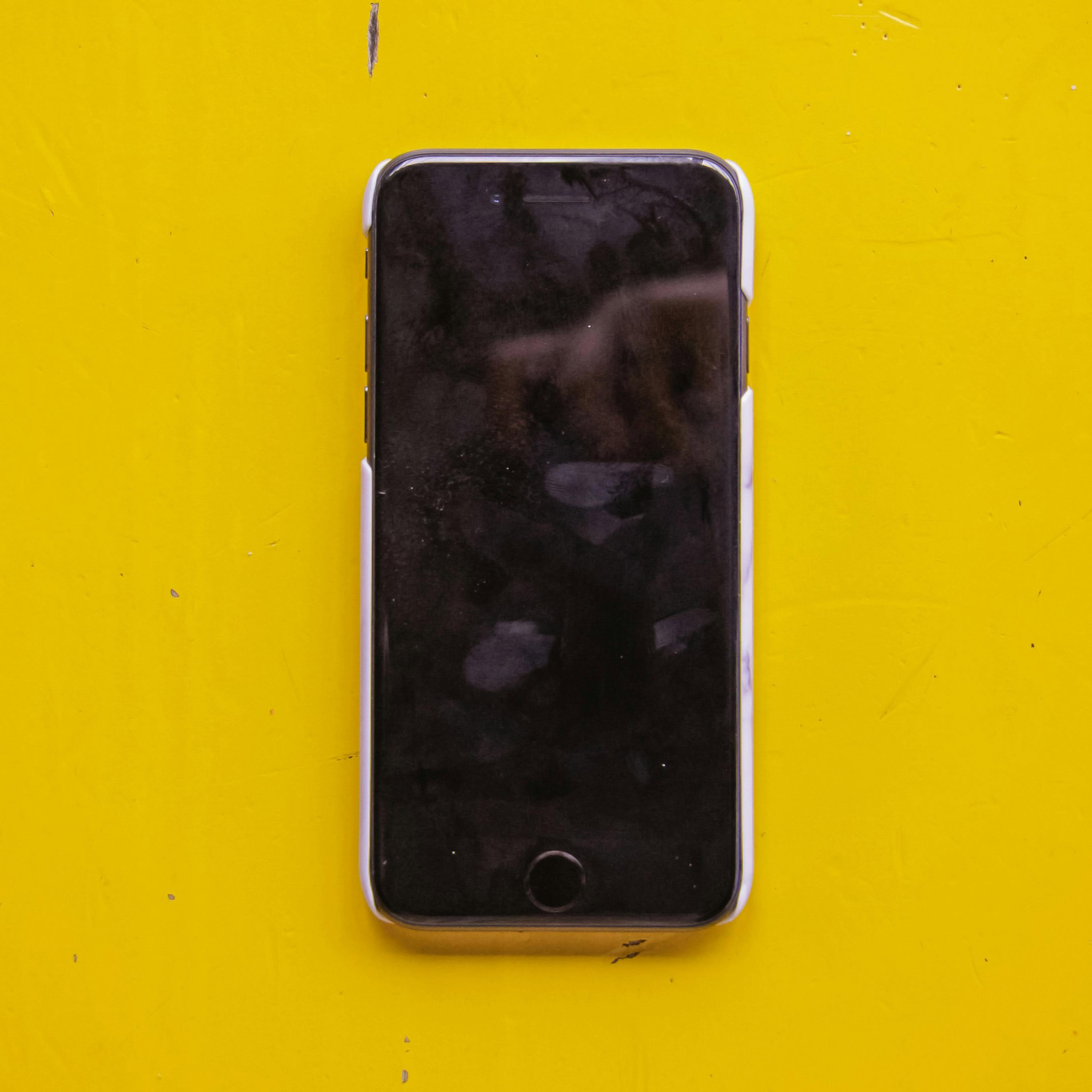 A switched-off smartphone on a bright yellow surface with fingerprints and smudges on the black screen.