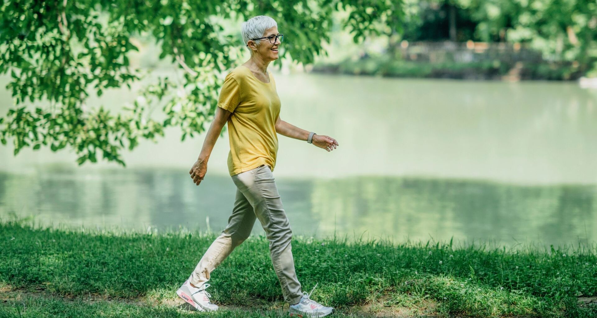 older woman walking on grass with a body of water behind her
