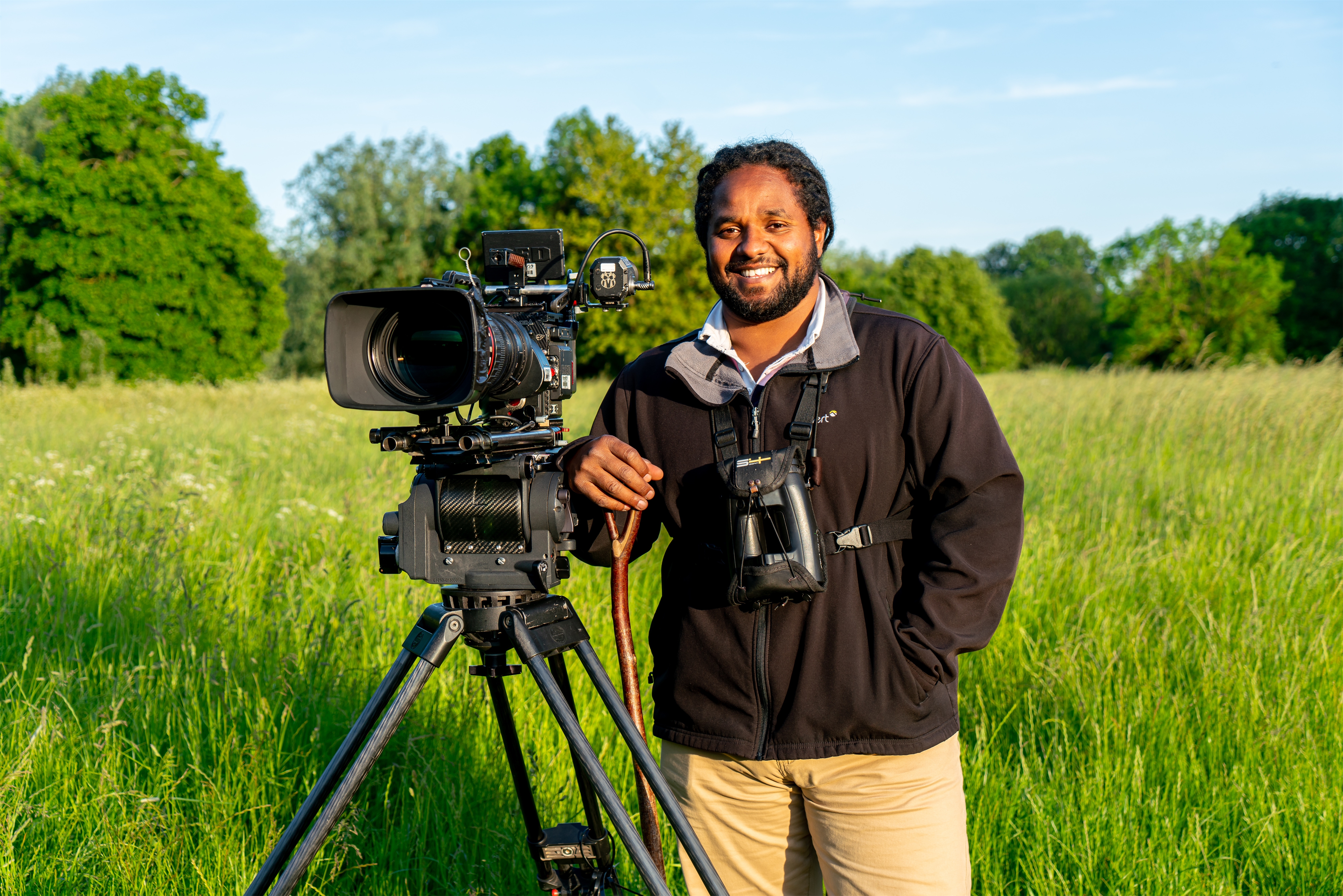 Hamza Yassin standing next to a camera in a field.