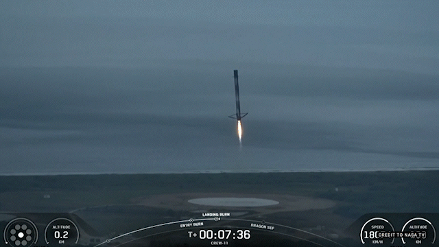A SpaceX rocket booster descending to a landing pad with a bright orange flame from its engine.
