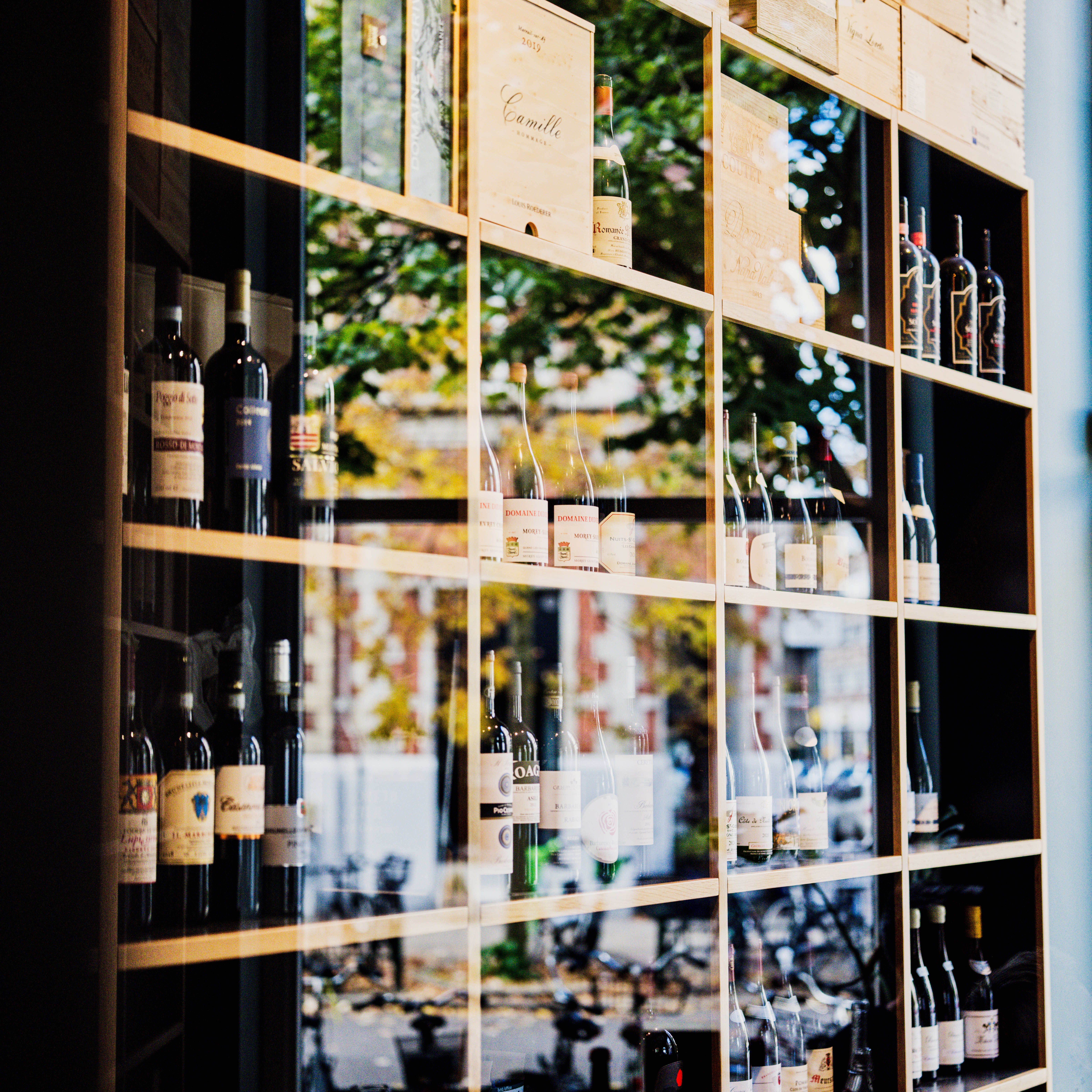A wine rack filled with bottles of wine and wooden wine crates, with reflections of a street scene visible through the glass.