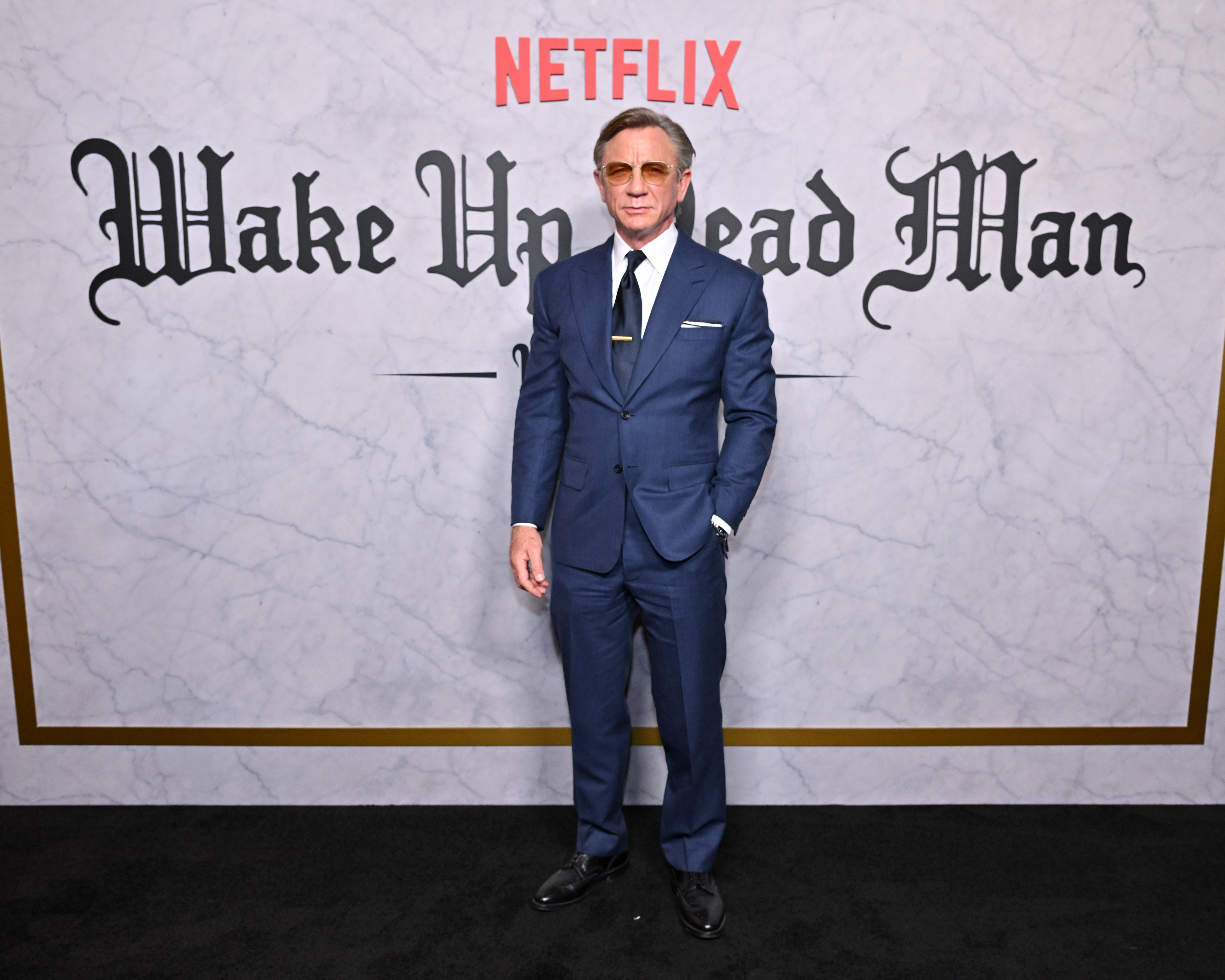 Daniel Craig in a blue suit and amber sunglasses at the Wake Up Dead Man NY Special Screening.