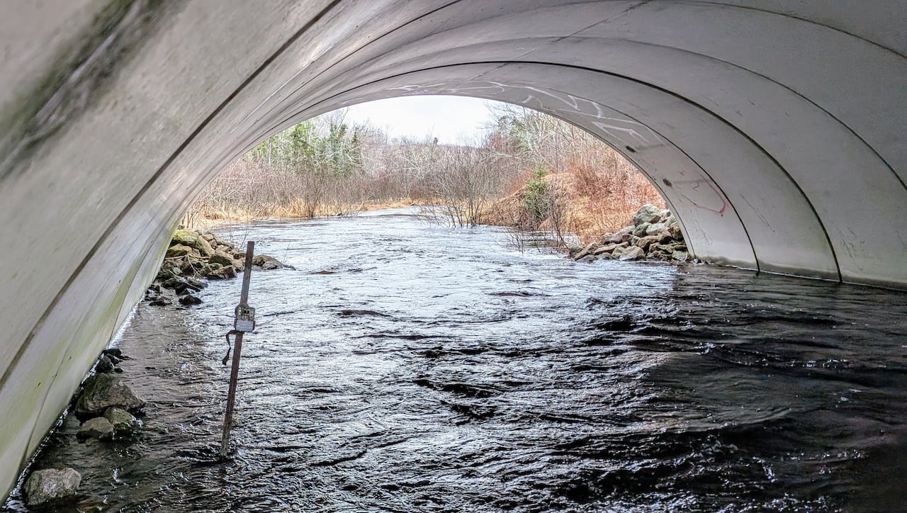 A camera on a post in a culvert full of rushing water.