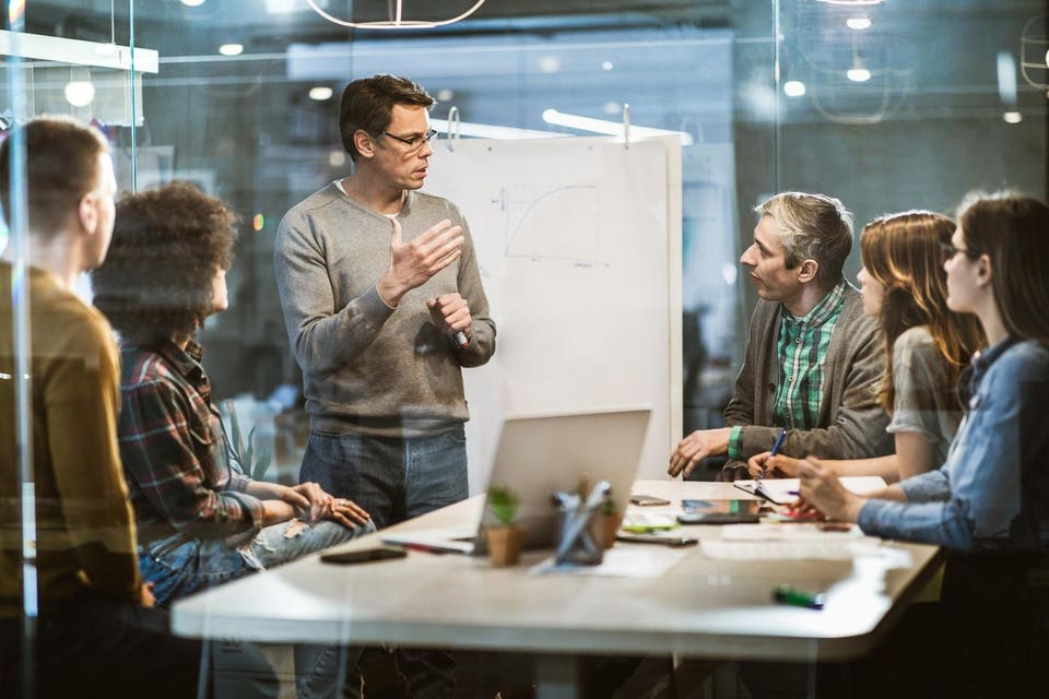 Mid adult businessman talking to his colleagues on presentation in the office.