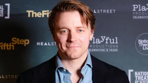 Getty Images A portrait shot of Jack Lowden at the premiere of The Fifth Step in Edinburgh, with a wall bearing the logos of sponsors behind him.