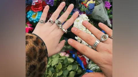 Sam Bok The hands of a couple at the Black Sabbath bridge. We can see the lady's engagement ring as well as all the other rings on her finger. We can see the Black Sabbath bridge behind her.
