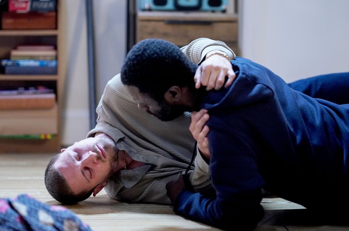 533754,TITLE:Eastenders Kojo helps a fragile Harry, who is lay on the floor, in EastEnders