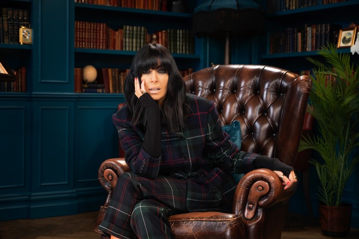 Claudia Winkleman sat down on a brown leather chair, resting her hand on her face.