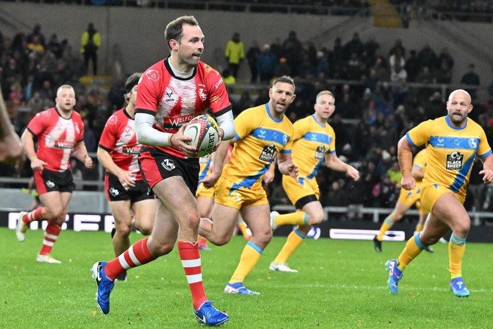 Andy Forsyth, in red and black rugby kit, runs with a rugby ball at The 745 Game.