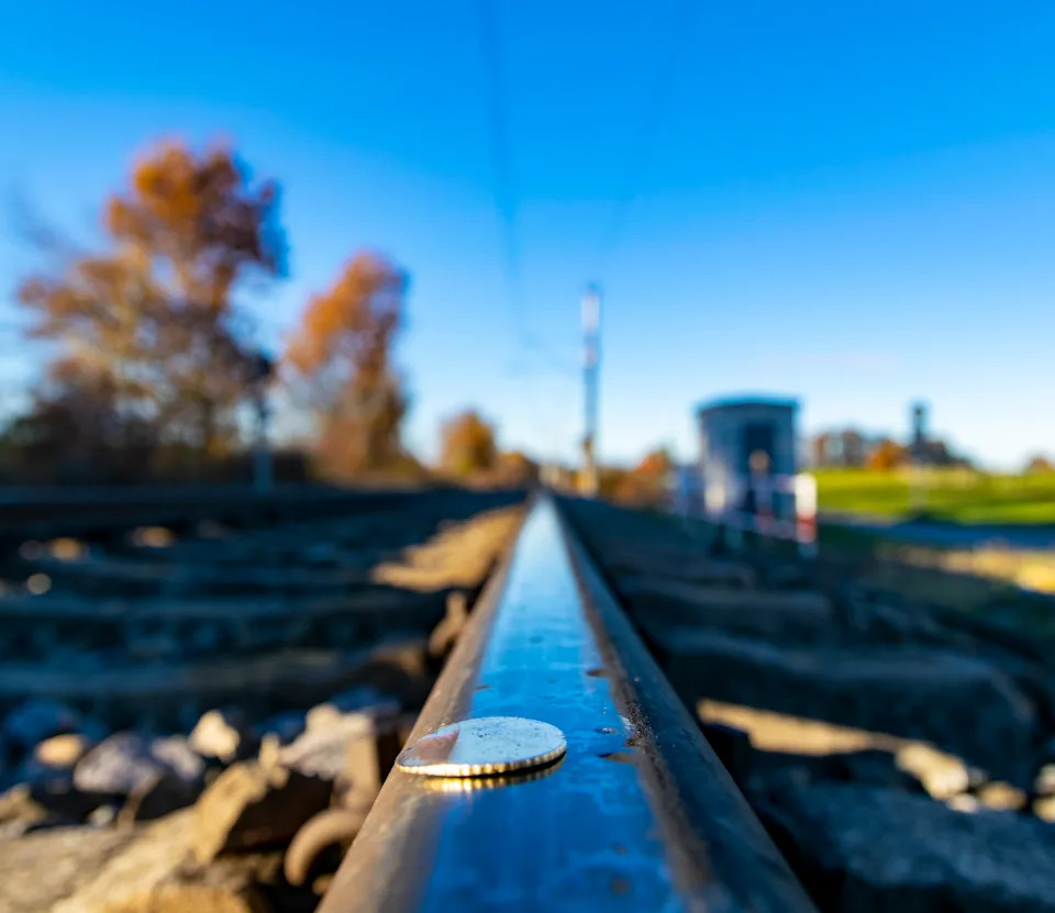 Coin on a railway track with a blurred background of trees and a station, symbolizing balance and adventure