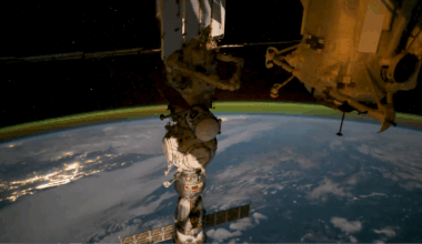 a green glow floats above earth in the background as a cylindrical space station module dominates the foreground